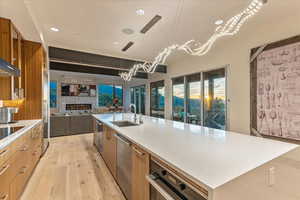 Kitchen featuring modern cabinets, a sink, a stone fireplace, brown cabinets, and light wood finished floors
