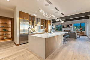 Kitchen with a sink, wall chimney range hood, a stone fireplace, light countertops, and high end refrigerator