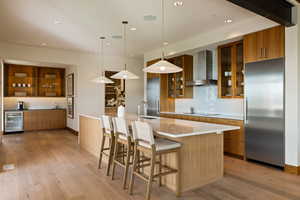 Kitchen with wall chimney exhaust hood, built in fridge, beverage cooler, brown cabinetry, and a sink