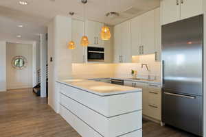 Kitchen featuring stainless steel appliances, wood finished floors, a peninsula, a sink, and white cabinets