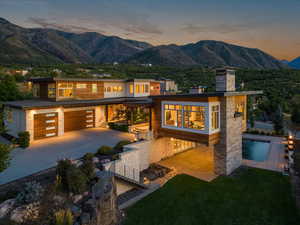 Back of house at dusk featuring concrete driveway, a mountain view, a chimney, stone siding, and a garage