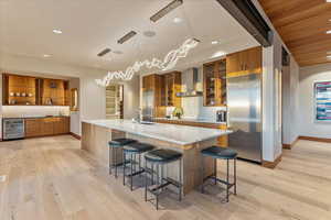 Kitchen featuring a sink, wall chimney range hood, built in fridge, brown cabinetry, and beverage cooler