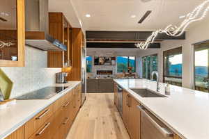 Kitchen with brown cabinetry, wall chimney range hood, dishwasher, a sink, and black electric cooktop