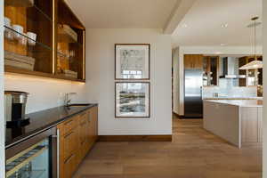 Bar featuring wall chimney exhaust hood, beverage cooler, stainless steel fridge, a sink, and baseboards