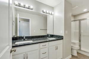 Full bathroom featuring double vanity, a sink, a stall shower, and toilet