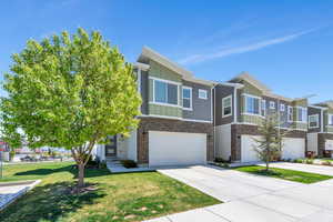 Multi unit property with a front yard, stone siding, board and batten siding, an attached garage, and driveway