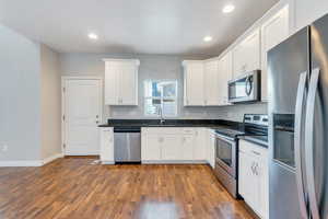 Kitchen featuring white cabinets, a sink, stainless steel appliances, recessed lighting, and dark wood-type flooring