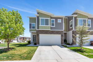 View of front of property featuring a front lawn, stone siding, board and batten siding, an attached garage, and driveway