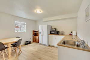 Kitchen with white cabinets, a sink, white refrigerator with ice dispenser, light wood-style floors, and light countertops