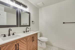 Bathroom with double vanity, toilet, baseboards, and a sink
