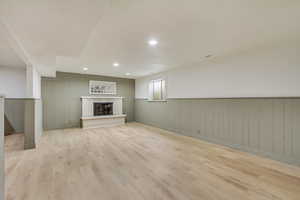 Basement with light wood-style floors, a wainscoted wall, a fireplace, and recessed lighting