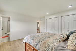 Bedroom featuring ensuite bath, baseboards, two closets, light wood finished floors, and recessed lighting