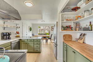 Kitchen with green cabinetry, open shelves, stainless steel appliances, range hood, and butcher block counters