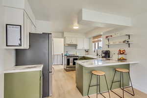 Kitchen with light countertops, stainless steel appliances, a peninsula, a kitchen bar, and under cabinet range hood