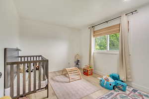 Bedroom with baseboards, a nursery area, and wood finished floors