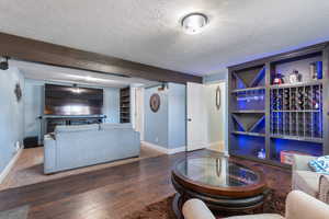 Living room featuring a textured ceiling, built in shelves, baseboards, and wood finished floors