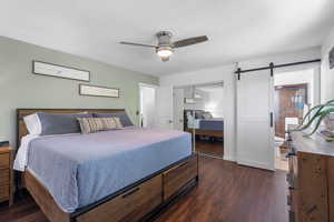 Bedroom with a closet, baseboards, a barn door, a ceiling fan, and dark wood finished floors