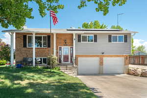 Raised ranch with roof mounted solar panels, an attached garage