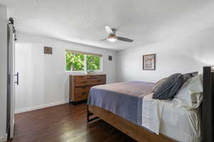 Bedroom featuring baseboards, ceiling fan, dark wood-type flooring, a barn door, and a textured ceiling