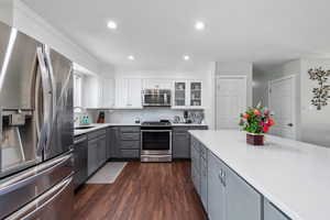 Kitchen with dark wood-style flooring, gray cabinetry, light countertops, a sink, and stainless steel appliances