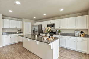Kitchen featuring white cabinets, a sink, light wood finished floors, dark stone counters, and stainless steel appliances