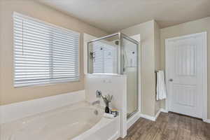 Bathroom featuring baseboards, a shower stall, wood finished floors, and a bath