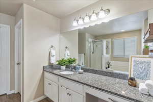 Full bath featuring vanity, baseboards, wood finished floors, a bath, and a stall shower
