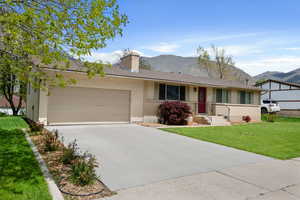Ranch-style house with a mountain view, a chimney, an attached garage, and a front lawn