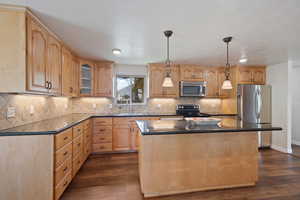 Kitchen featuring dark countertops, a sink, light brown cabinets, a center island, and stainless steel appliances