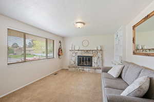 Living room with a textured ceiling, visible vents, a fireplace, baseboards, and carpet flooring