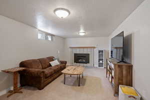Carpeted living area with a brick fireplace, a textured ceiling, and baseboards