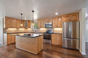 Kitchen with dark wood-style flooring, a kitchen island, dark countertops, a sink, and appliances with stainless steel finishes