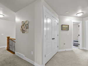 Hallway with light carpet, baseboards, visible vents, and an upstairs landing