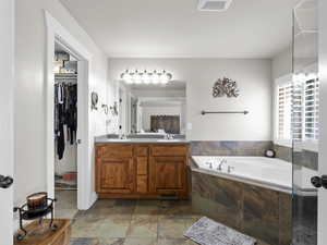 Bathroom featuring a sink, a bath, a spacious closet, double vanity, and stone finish flooring