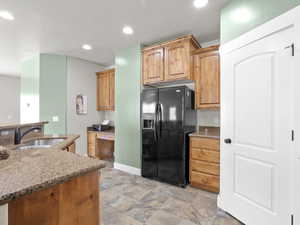 Kitchen with a sink, black fridge with ice dispenser, light stone countertops, stone finish floor, and recessed lighting