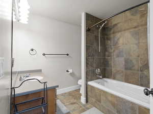 Bathroom with tiled shower / bath, vanity, stone tile flooring, baseboards, and toilet