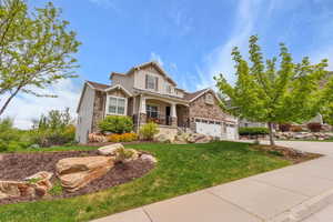 Craftsman house featuring stone siding, board and batten siding, a front yard, covered porch, and driveway