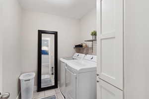 Washroom with laundry area, washing machine and dryer, and light tile patterned floors