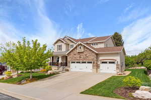 Craftsman-style house with an attached garage, a front lawn, driveway, and stone siding