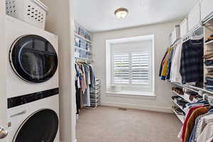 Laundry room featuring laundry area, visible vents, stacked washing maching and dryer, carpet floors, and baseboards