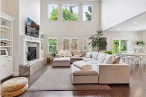 Living room with a towering ceiling, a tiled fireplace, built in features, dark wood finished floors, and recessed lighting