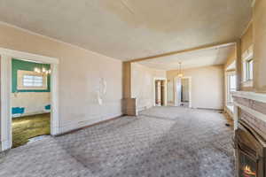 Unfurnished living room with carpet floors, a textured ceiling, a notable chandelier, and a fireplace