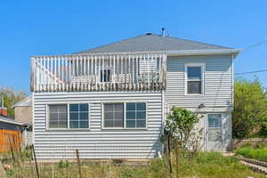 Back of property with a shingled roof, fence, and a balcony