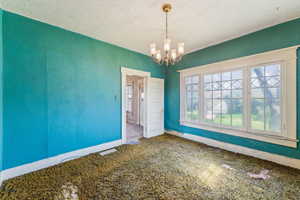 Carpeted empty room with baseboards, a textured ceiling, and a chandelier