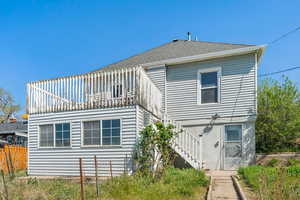 Rear view of property featuring fence, stairs, and roof with shingles