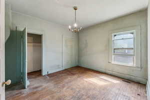 Unfurnished bedroom featuring visible vents, two closets, a notable chandelier, and hardwood / wood-style floors