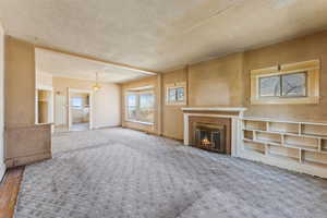 Unfurnished living room with a glass covered fireplace, carpet floors, and a textured ceiling