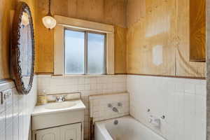 Bathroom with a garden tub, tile walls, and vanity