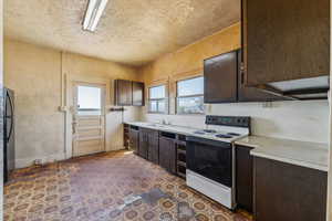 Kitchen featuring a sink, light countertops, electric range, and dark brown cabinets