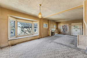 Unfurnished living room featuring carpet floors, a textured ceiling, a healthy amount of sunlight, and an inviting chandelier